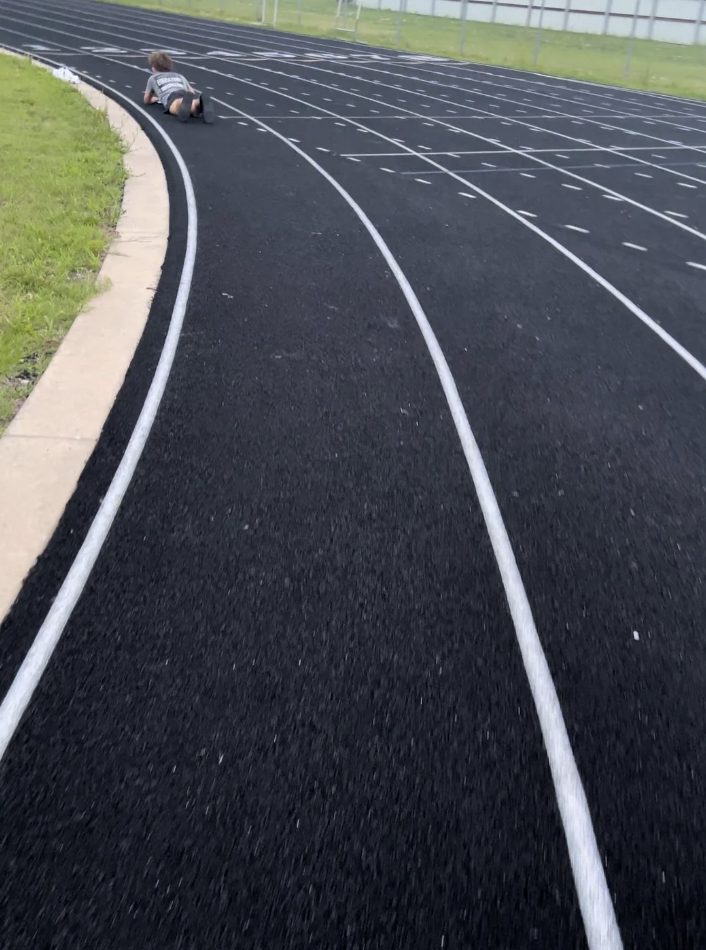 Child lying on a track field, with a comedic pose suggesting a sudden halt in motion