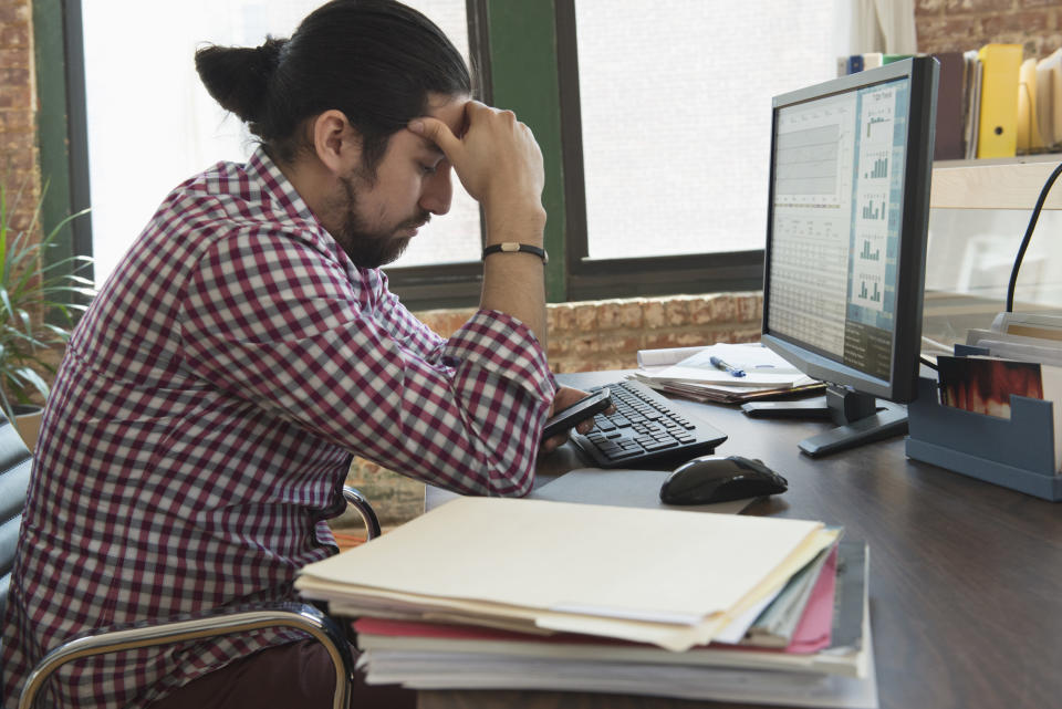 A man looks overwhelmed as he works at his office desk