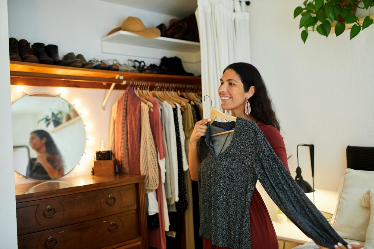 Smiling woman choosing a dress to wear while standing by a closet in her bedroom at home