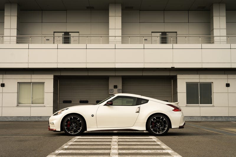 a white nissan fairlady z nismo parked in front of the garages at a race track in japan