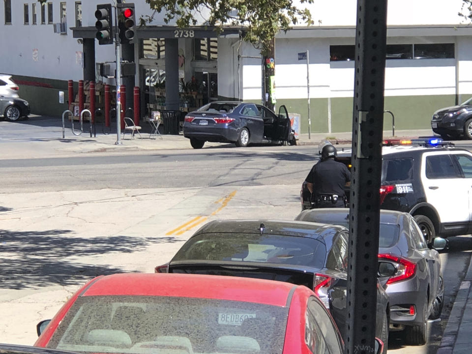 <p>Police officers stand guard near a crashed vehicle outside a Trader Joe’s store in the Silver Lake neighborhood of Los Angeles on Saturday. Police believe a man involved in the standoff with officers shot his grandmother and girlfriend before firing at officers during a pursuit, then crashing outside the supermarket and running inside the store. (Photo: Christian Dunlop via AP) </p>