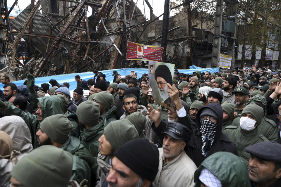 A poster of Supreme Leader Ayatollah Khamenei is held up as mourners attend a funeral procession of Revolutionary Guard member Morteza Ebrahimi, while passing buildings which were damaged in recent protests in Shahriar, Iran, Wednesday, Nov. 20, 2019. Ebrahimi was killed during protests over government-set fuel prices rising last week, demonstrations that quickly spiraled in violence. (AP Photo/Vahid Salemi)