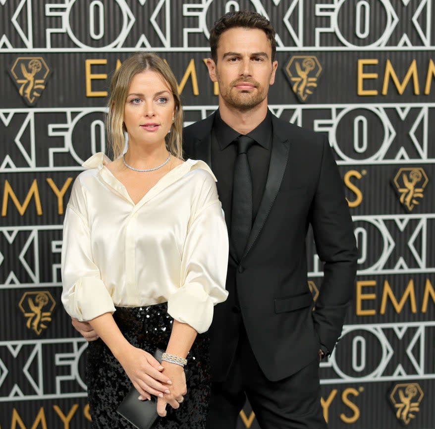 Ruth Kearney wearing a white blouse and black sequined skirt, and Theo James in a black suit on the red carpet at the Emmys