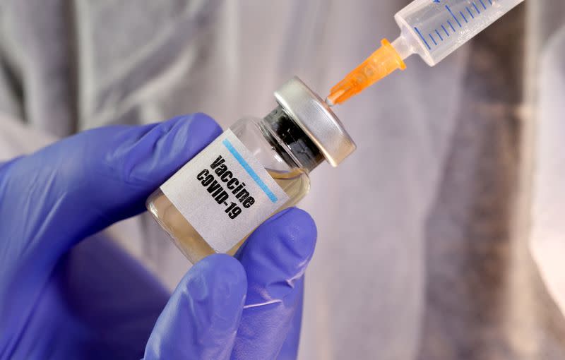 FILE PHOTO: A woman holds a small bottle labeled with a "Vaccine COVID-19" sticker and a medical syringe in this illustration