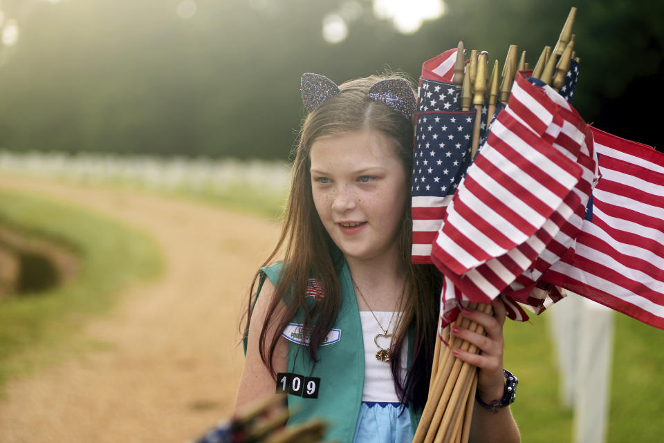 <p>Girl Scout Caitlyn Hootsell, 10, carries a bundle of U.S. flags, Saturday, May 26, 2018 for placement in front of tombstones at the Natchez National Cemetery in Natchez, Miss., as the community honors those who died in service to their country. (Photo: Nicole Hester/The Natchez Democrat via AP) </p>