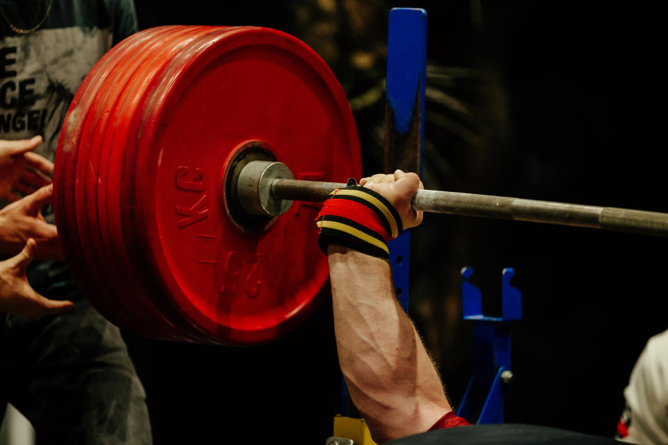 muscular hand male powerlifter bench press barbell with red plates