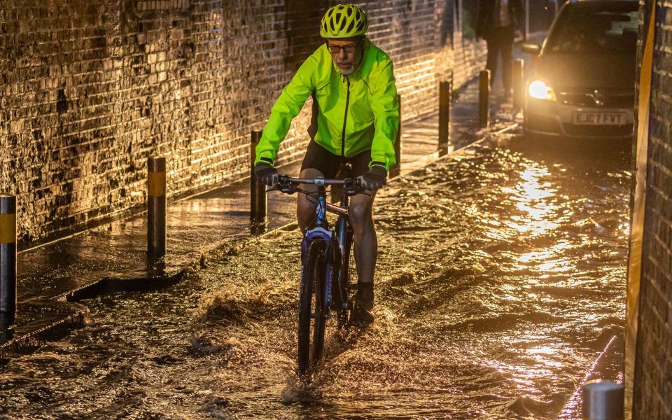 After a night of torrential rain, a cyclist gets caught in flooding this morning in Wimbledon, south-west London