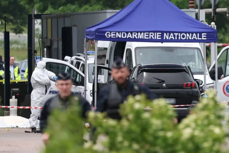 A forensic doctor works as police officers patrol the scene of a ram raid that took place late this morning at a toll booth in Incarville in the Eure region of northern France. Police officers were killed and others injured in an attack on a prisoner transport in the north of France. Alain Jocard/AFP/dpa