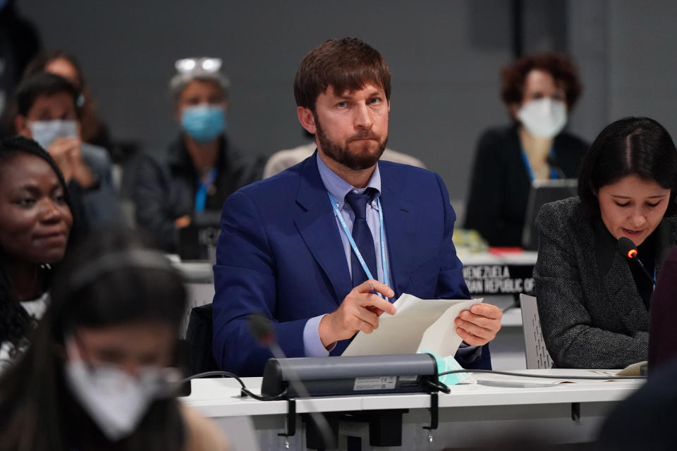 Delegates at the COP26 climate summit, some wearing face masks, sit at tables outfitted with name plaques and speakers.