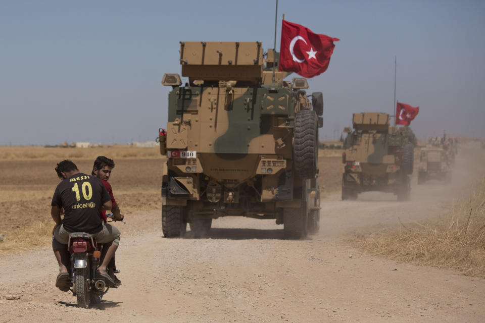 Two men on a motorbike follow Turkish and American forces as they conduct their first joint ground patrol in the so-called "safe zone" on the Syrian side of the border with Turkey, seen in the background, near Tal Abyad, Syria, Sunday, Sept. 8, 2019. Turkey hopes the buffer zone, which it says should be at least 30 kilometers (19 miles) deep, will keep Syrian Kurdish fighters, considered a threat by Turkey but U.S. allies in the fight against the Islamic State group, away from its border. (AP Photo/Maya Alleruzzo)