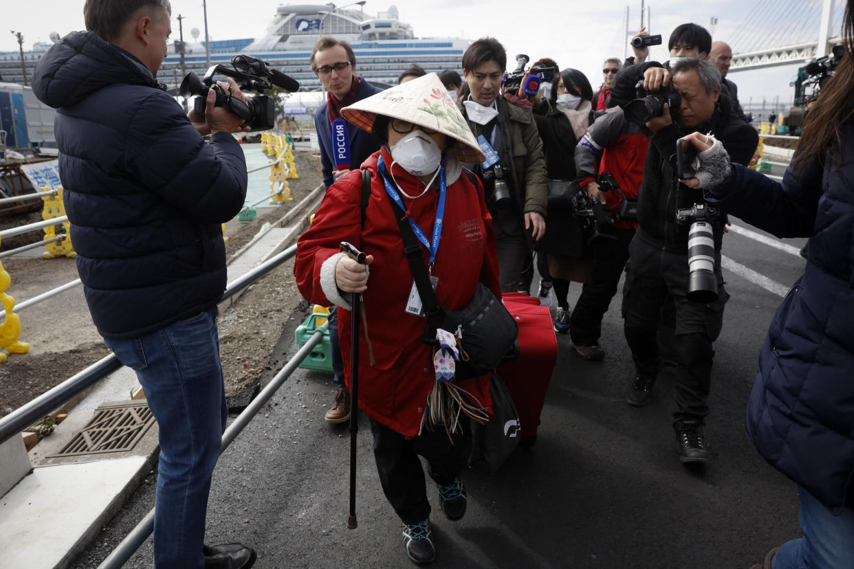 An unidentified passenger is surrounded by the media after she disembarked from the quarantined Diamond Princess cruise ship Wednesday, Feb. 19, 2020, in Yokohama, near Tokyo. Passengers tested negative for COVID-19 started disembarking Wednesday. (AP Photo/Jae C. Hong)