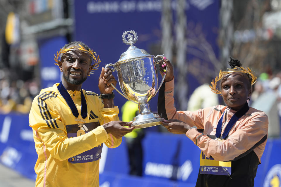 Sisay Lemma, of Ethiopia, left, winner of the men's division of the Boston Marathon, and Hellen Obiri, of Kenya, right, winner of the women's division of the race, hold the trophy on the finish line of the Boston Marathon, Monday, April 15, 2024, in Boston. (AP Photo/Steven Senne)