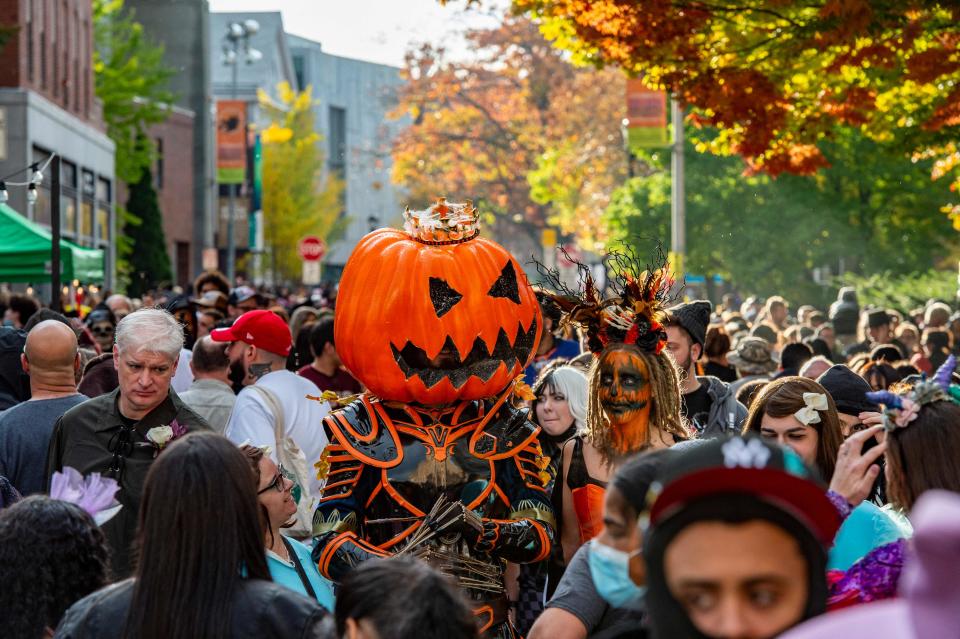 A large pumpkin-headed costumed reveller walks with others through a crowded street on Halloween in Salem, Massachusetts on October 31, 2021.