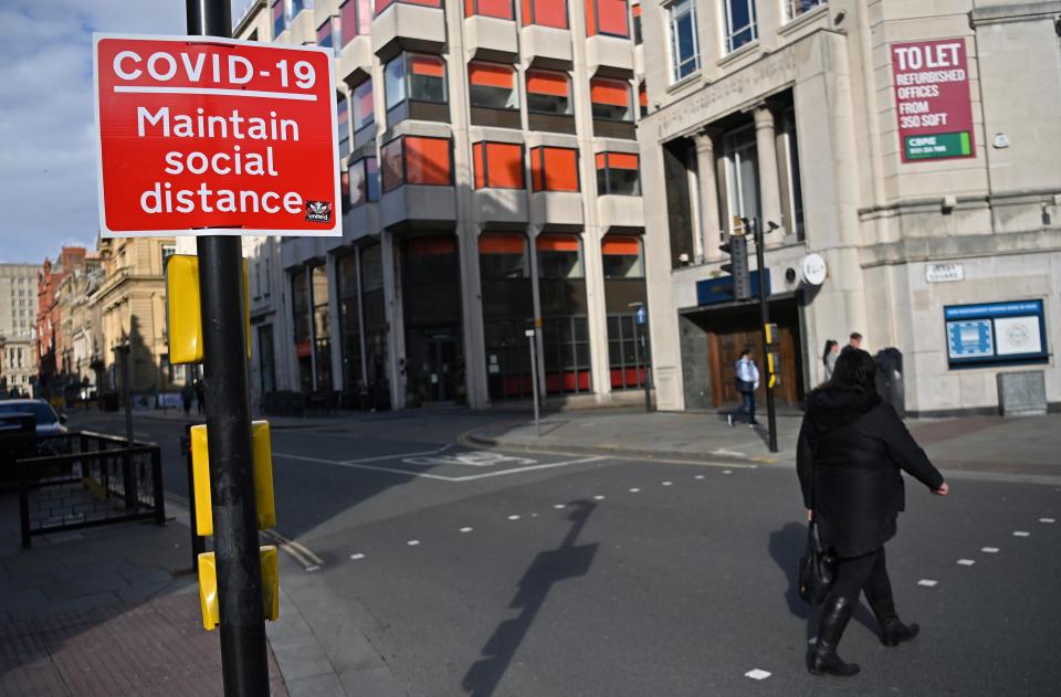 A pedestrian passes a Social Distancing sign as they cross an empty road in Liverpool, north west England on October 14, 2020, as new local lockdown measures come in to force to help stem a second wave of the novel coronavirus COVID-19. - The northwest English city of Liverpool was the first to be put in the government's new the highest risk category, with a ban on household mixing and pub closures coming into force Wednesday for at least four weeks. (Photo by Paul ELLIS / AFP) (Photo by PAUL ELLIS/AFP via Getty Images)