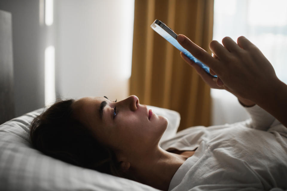 Woman lying in bed looking at her phone, appearing thoughtful