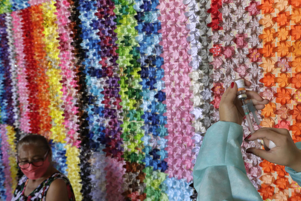 FILE - In this March 29, 2021 file photo, a health worker prepares a shot of the Sinovac vaccine for COVID-19 in front of a panel of origami lotus flowers, placed in honor of victims of the pandemic, at a health center in Brasilia, Brazil. According to the organizers, the flower panel is also a gesture of thanks to health professionals and of hope to those who are being vaccinated. (AP Photo/Eraldo Peres, File)