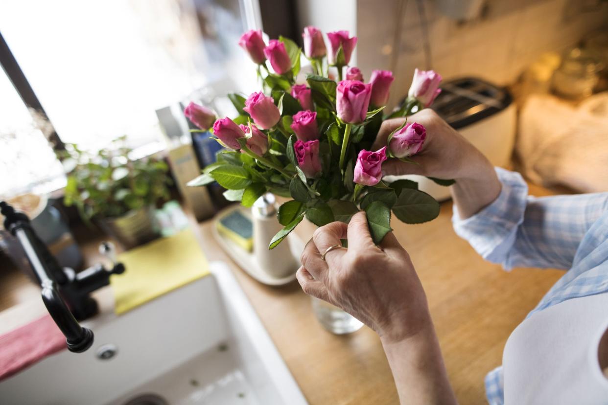 Unrecognizable senior woman at home in her kitchen arranging roses in vase