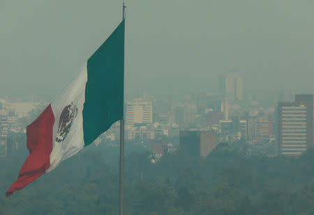 A general view shows a Mexico flag against hazy backdrop of buildings in metropolitan Mexico City May 14, 2019 as Mexico authorities declared an environmental emergency on Tuesday for metropolitan Mexico City, as smoke from nearby wildfires pushed pollution to levels deemed potentially harmful to human health. Picture taken through a glass window. REUTERS/Henry Romero