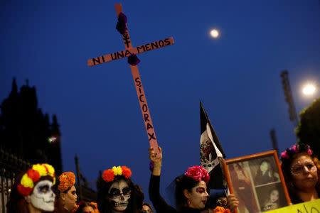 An activist with her face painted to look like the popular Mexican figure "Catrina" holds a cross as she takes part in a march against femicide during the Day of the Dead in Mexico City, Mexico November 1, 2017. Cross reads "No one more". REUTERS/Carlos Jasso