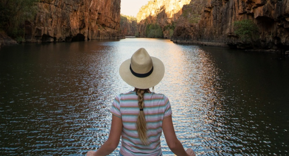 A Tourism NT publicity still showing a woman in a hat with her back to the camera. She's looking across a water filled gorge.