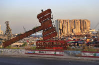 FILE - In this Aug. 4, 2021 file photo, a monument that represents justice stands in front of towering grain silos that were gutted in the massive August 2020 explosion at the port that killed more than 200 people and wounded over 6,000, in Beirut, Lebanon. For eight months Tarek Bitar, a relatively obscure judge has quietly investigated one of the world's worst non-nuclear explosions with only two assistants helping him -- and a lot of powerful detractors blocking him. For many Lebanese Bitar is their only hope for truth and accountability in a country that craves both. But for the country's entrenched political class, the 47-year-old Bitar has become a nightmare that needs to be dealt with. (AP Photo/Hussein Malla, File)