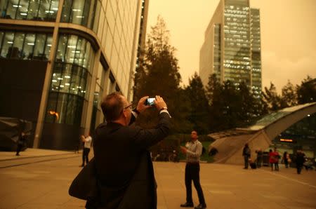 A man photographs the sky turning red over buildings in Canary Wharf as dust from the Sahara carried by storm Ophelia filters sunlight over London. REUTERS/Tom Jacobs