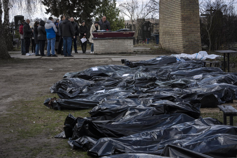 A family mourns a relative killed during the war with Russia, as dozens of black bags containing more bodies of victims are seen strewn across the graveyard in the cemetery in Bucha, in the outskirts of Kyiv, Ukraine, Monday, April 11, 2022. (AP Photo/Rodrigo Abd)