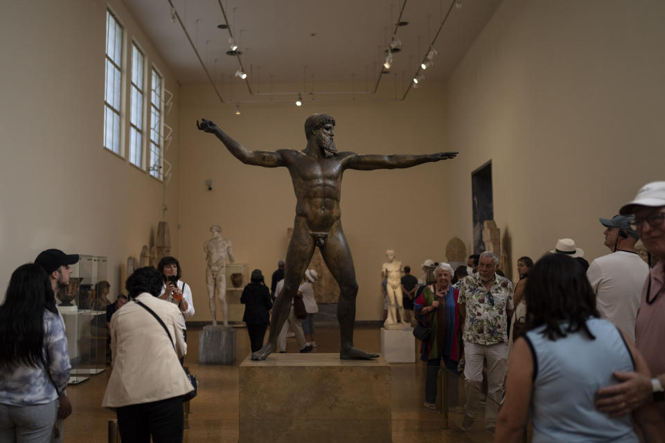 Tourists admire the seven-foot bronze statue of Zeus, or Poseidon, made in the mid-5th century B.C. at the archaeological museum of Athens, on Tuesday, Oct. 4, 2022.The tourism industry in Greece and Portugal are expected to make a full recovery from the pandemic, while other EU members in the Mediterranean have also performed above the expectations of national governments. (AP Photo/Petros Giannakouris)