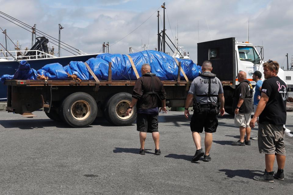 New Bedford and Fairhaven officials look on as a whale which was found dead in New Bedford harbor is taken away after it was placed on a truck at Union Wharf in New Bedford.