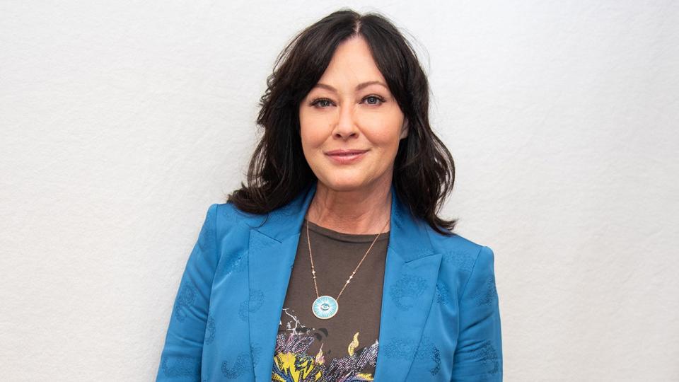 Shannen Doherty smiles in a blue blazer and a printed T-shirt