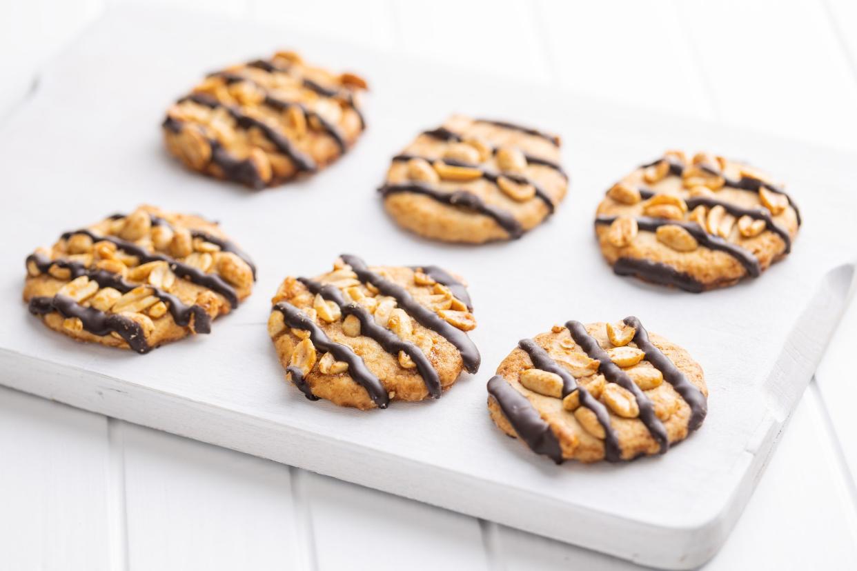 Chip cookies with peanuts and chocolate strips on a white table.