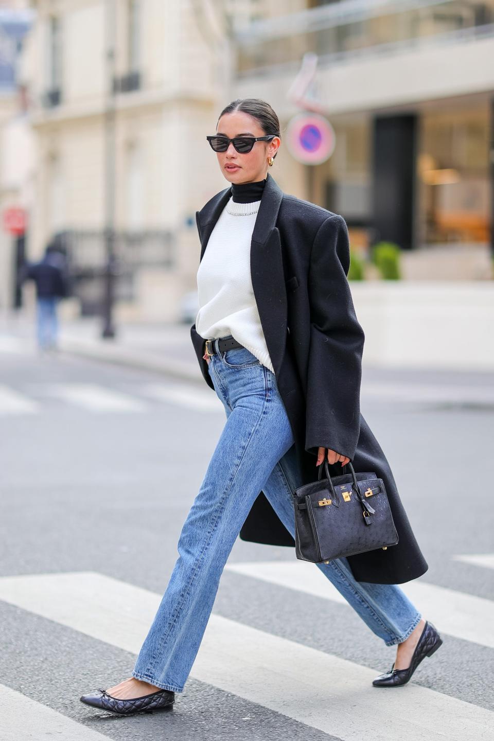 A women walking on a crossing in Paris, France, wearing jeans and a long black coat.