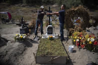 Cemetery worker Jorge Arvizu, left, helps a family member place a plaque on the grave of Vicente Dominguez who died of complications related to the new coronavirus, at the municipal cemetery Valle de Chalco, on the outskirts of Mexico City, Tuesday, Oct. 20, 2020. Mexican families traditionally flock to local cemeteries to honor their dead relatives as part of the “Dia de los Muertos,” or Day of the Dead celebrations, but according to authorities the cemeteries will be closed this year to help curb the spread of COVID-19. (AP Photo/Marco Ugarte)