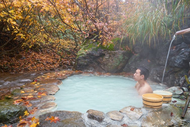 A man sits in a milky pool of hot water underneath autumn foliage.