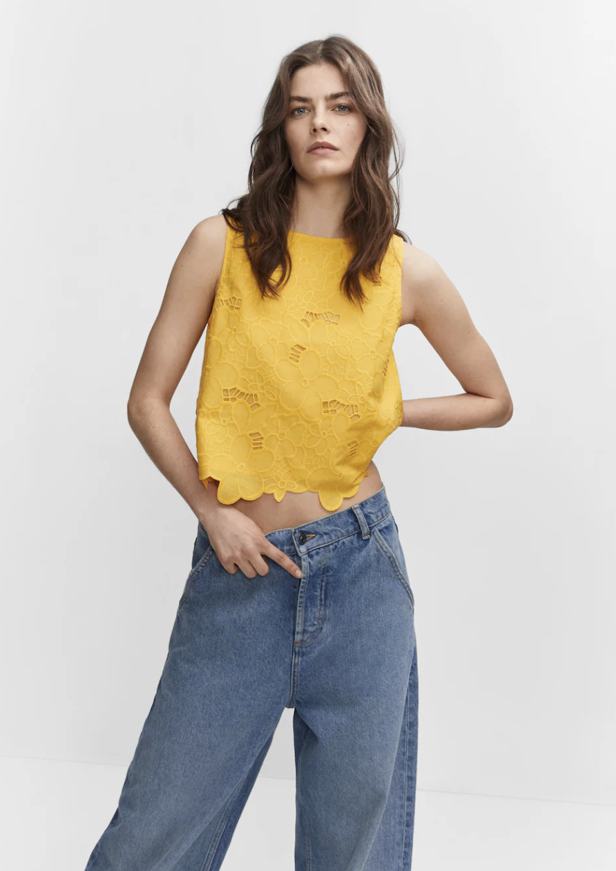 brunette model wearing blue jeans and yellow Embroidered openwork blouse (Photo via Mango)