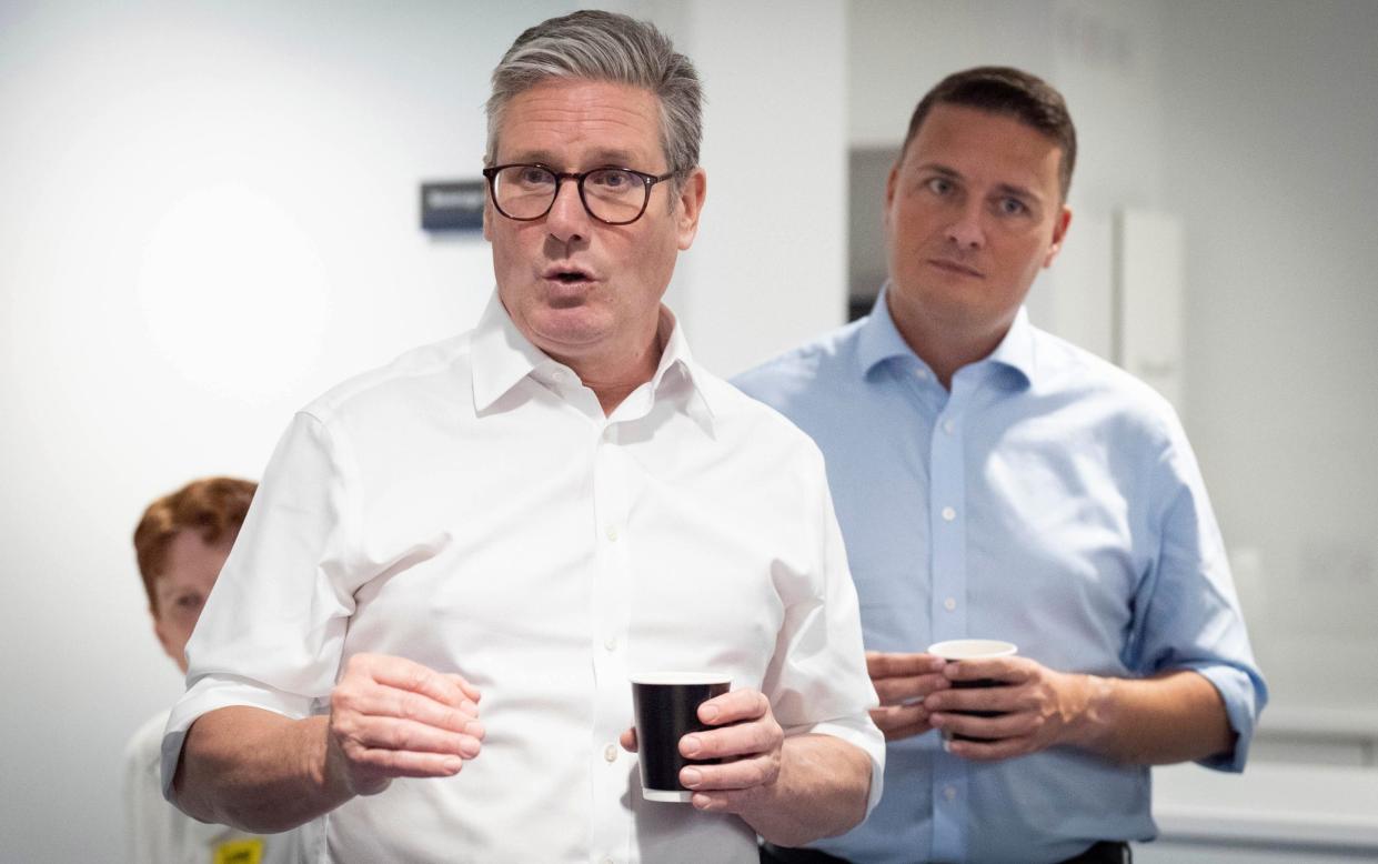 The two men hold takeaway coffee cups and wear their shirtsleeves