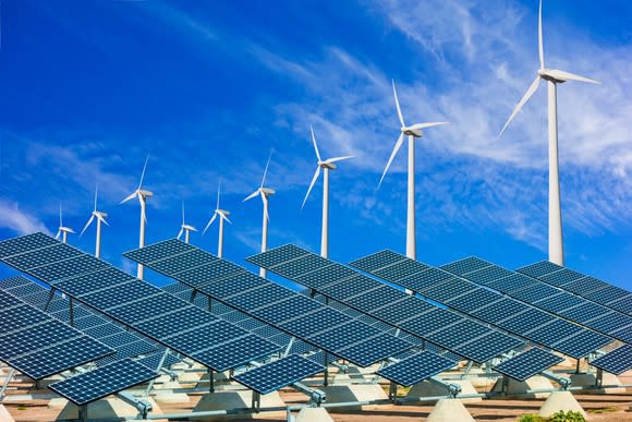 Solar farm with wind turbines in the background.