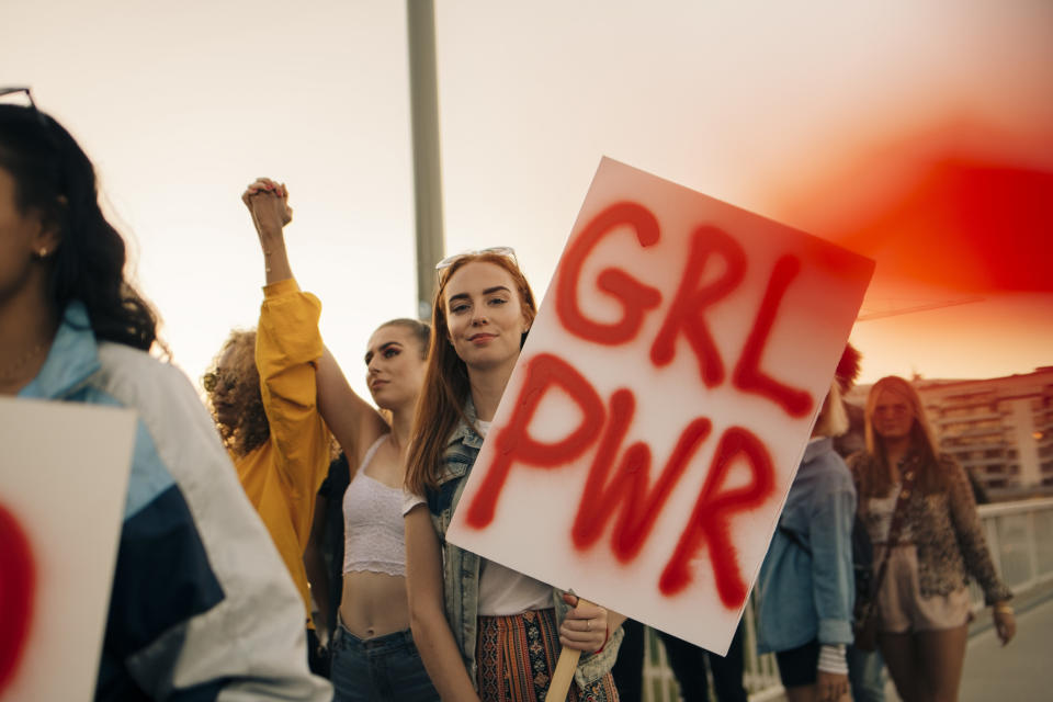 A group of individuals at a rally, one holding a sign with “GRL PWR” written on it, embodying empowerment