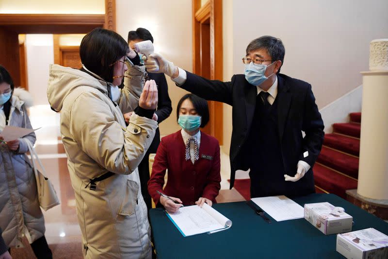 A man uses a thermometer to check the temperature of a journalist covering a meeting between Tedros Adhanom, director general of the World Health Organization, and Chinese Foreign Minister Wang Yi at the Diaoyutai State Guesthouse in Beijing