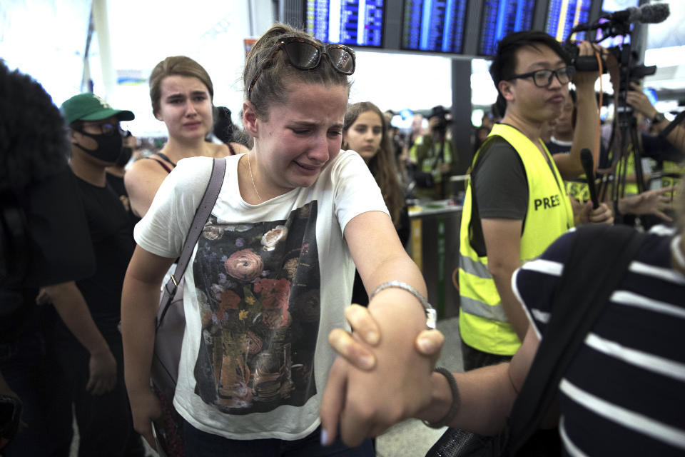Travelers react as they manage to walk through the protesters to the departure gates during a demonstration at the Hong Kong International Airport in Hong Kong, Tuesday, Aug. 13, 2019. Protesters severely crippled operations at Hong Kong's international airport for a second day Tuesday, forcing authorities to cancel all remaining flights out of the city after demonstrators took over the terminals as part of their push for democratic reforms. (AP Photo/Vincent Thian)