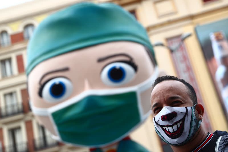 A man wearing a protective face mask poses for pictures next to an oversized model of a health worker in Madrid