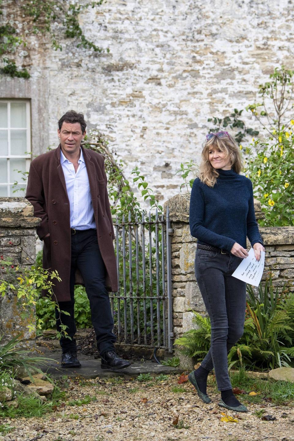 A man and wife holding a piece of paper stand outside a home. 