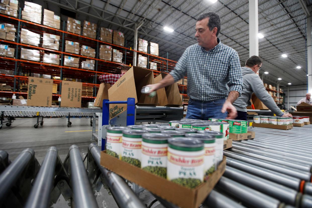 Mike Goodhartt and other workers at the L.L. Bean shipping center box up donated canned foods to be distributed for food pantries across the state of Maine, Tuesday, March 24, 2020, in Freeport, Maine. The outdoor retailer, which is experiencing sinking sales because of coronavirus, is partnering with the Good Shepherd food bank.