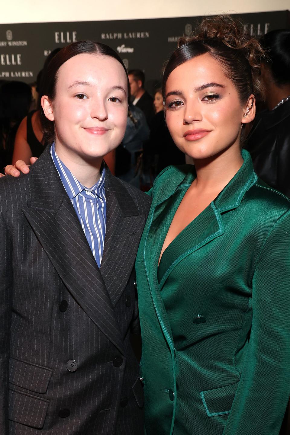 Bella Ramsey and Isabela Merced posing, one in a pinstripe suit, the other in a green suit, at a formal event