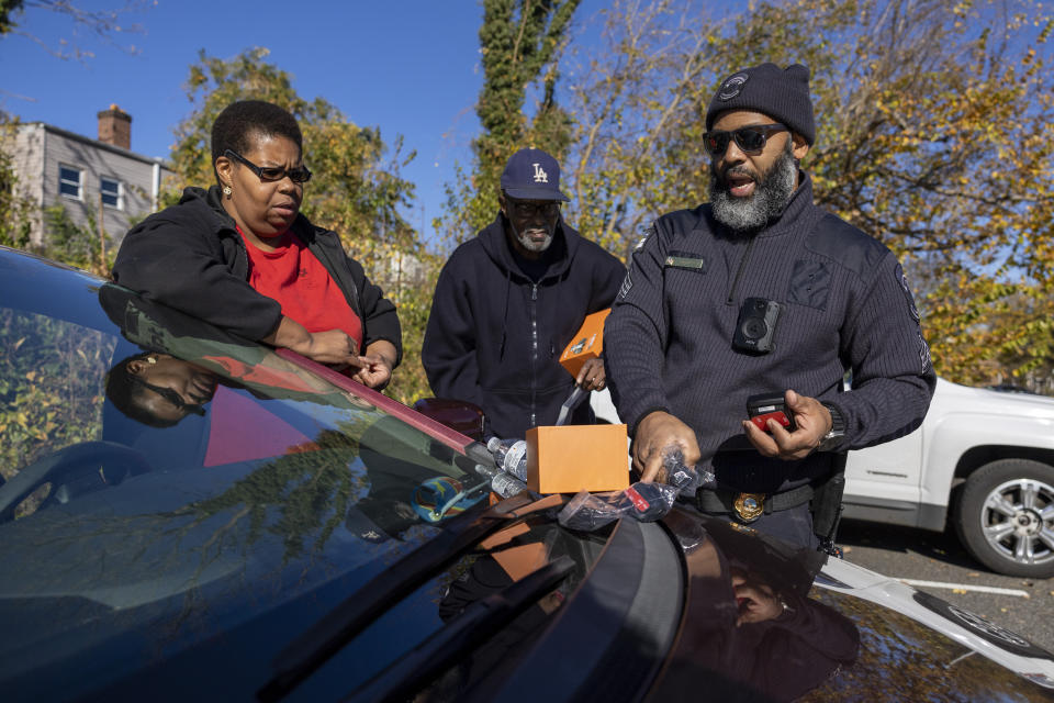 Sgt. Jason Godfrey explains to Grace Jdemba, a delivery driver, and Bernard, who did not give his last name, an Uber driver, how to use their cameras during an event where car cameras were distributed to drivers in an effort to combat a rise in crime, hosted in the parking lot of Robert F. Kennedy Stadium in Washington, Tuesday, Nov. 14, 2023. (AP Photo/Amanda Andrade-Rhoades)
