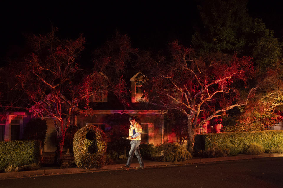 A Pacific Gas & Electric worker passes a home on Merrill Dr. in Moraga, Calif., as firefighters work to contain a wildfire burning behind it on Thursday, Oct. 10, 2019. Police ordered evacuations as the fast-moving wildfire spread in the hills of the San Francisco Bay Area community. The area is without power after Pacific Gas & Electric preemptively cut service to more than half a million customers hoping to prevent wildfires during dry, windy conditions. (AP Photo/Noah Berger)