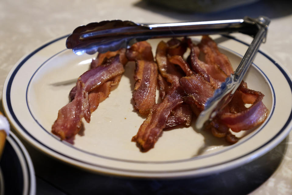 FILE - A plate of bacon sits on the kitchen table on the Ron Mardesen farm, Thursday, Dec. 2, 2021, near Elliott, Iowa. A 2018 voter-approved California ballot measure, to take effect, Jan. 1, 2022, set the nation's toughest living space standards for breeding pigs. Critics have called for putting off enforcement until 2024 for fear prices will rise and jobs will be lost. Mardesen already meets the California standards for the hogs he sells to specialty meat company Niman Ranch, which supported passage of Proposition 12 and requires all of its roughly 650 hog farmers to give breeding pigs far more room than mandated by the law. (AP Photo/Charlie Neibergall,File)