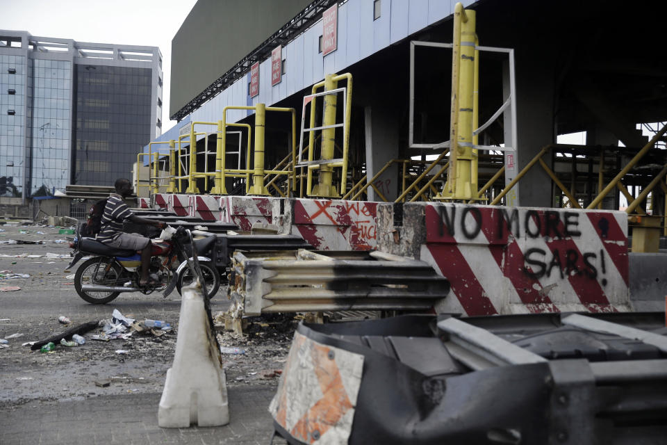 People drive past burnt toll gates with anti police slogans sprayed across, in Lagos Friday, Oct. 23, 2020. Resentment lingered with the smell of charred tires Friday as Nigeria's streets were relatively calm after days of protests over police abuses, while authorities gave little acknowledgement to reports of the military killing at least 12 peaceful demonstrators earlier this week. (AP Photo/Sunday Alamba)