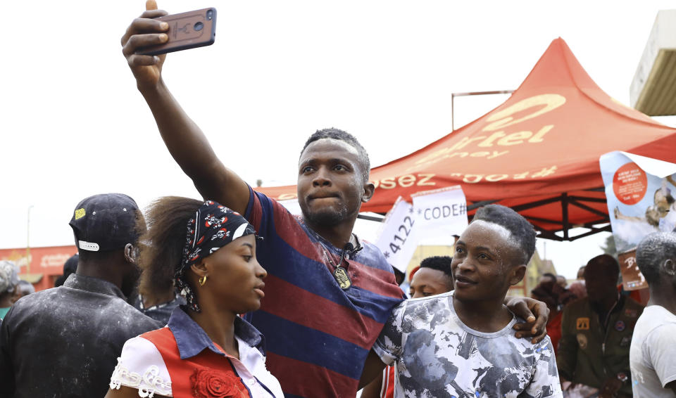 In this photo of Wednesday, Sept.11, 2019, Congolese student and Ebola survivor Claude Mabowa, middle in striped red T-shirt with his friends. take a celfiein Beni, Congo. Mabowa managed to pass his college entrance exam while in isolation for treatment. Mabowa, who took them in July behind glass, said this week that this brings him hope he can still realize his dreams. (AP Photo/Al-hadji Kudra Maliro)