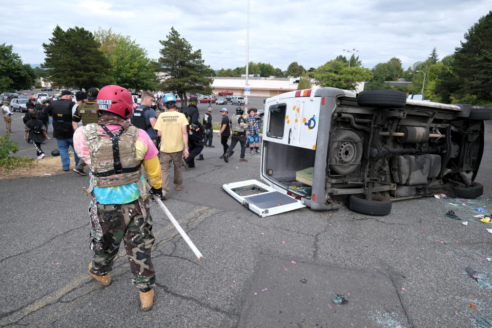 A van that was driven by anti-fascist protesters is pictured flipped on its side with all windows smashed after it was attacked for trying to drive into a Proud Boys rally Sunday, Aug. 22, 2021, in Portland, Ore. (AP Photo/Alex Milan Tracy)